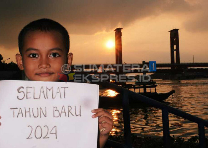TAHUN BARU 2024-Seorang anak membuat tulisan selamat tahun baru 2024 dari kawasan 9/10 Ulu Palembang dengan latarbelakang Jembatan Ampera dan sunset tanggal (31/12/2023). Foto: Budiman/Sumateraekspres.id