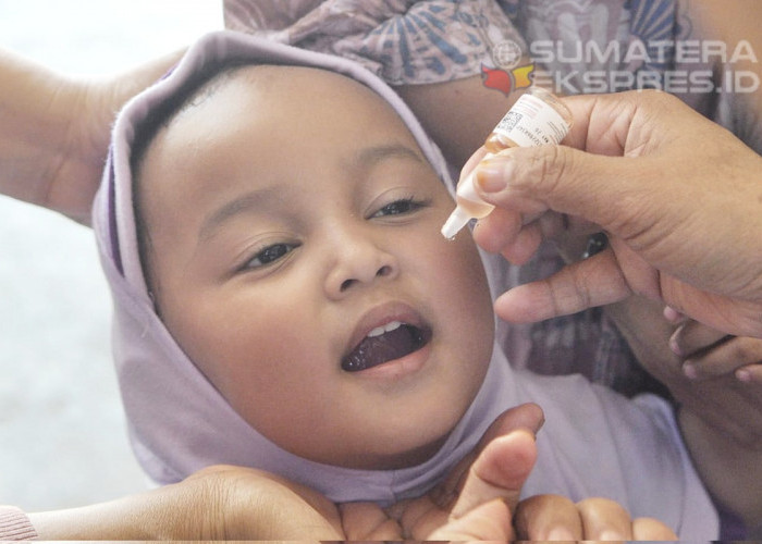 Buka Mulut - Seorang anak membuka mulutnya dengan didampingi orang tuanya dan tenaga kesehatan untuk meneteskan vaksin polio pada pencanangan Pekan Imunisasi Nasional Polio di Posyandu Delima Bukit Kecil Palembang. Foto: Budiman/Sumateraekspres.id